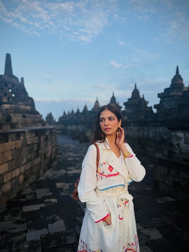 A couple of weeks back, I visited Borobudur, one of the largest Buddhist temples in the world. They said sunrise is the most magical time to experience it, before the tourist rush begins and when everything still feels calm and serene. So I, a self-proclaimed non-morning person woke up at 4am to go see this gorgeous temple, desperately hoping it was worth the early wake up effort. What I saw that morning was nothing short of magical. The temple slowly emerging with the first light, surrounded by lush tropical rainforests and framed by multiple volcanoes on almost all sides. So surreal and otherworldly. I racked my mind to think if I’d seen anything like this topography on any of my multiple other travels. I couldn’t think of any that came close to what this was. Knowing that Borobudur dates back to the 9th century, and that each level of the temple represents a journey toward enlightenment, added another layer to the experience. Walking through it at that hour, with barely anyone around, made it feel personal in a way that’s hard to describe. This one is going to be bookmarked in my travel diary as one of my favourite travel experiences :)♥️Also wearing this gorgeous jamdani coat from @indigo_dreams_ which is such a stunning way to incorporate a traditional Indian weave into my travel wardrobe ♥️ by @malavikamohanan_